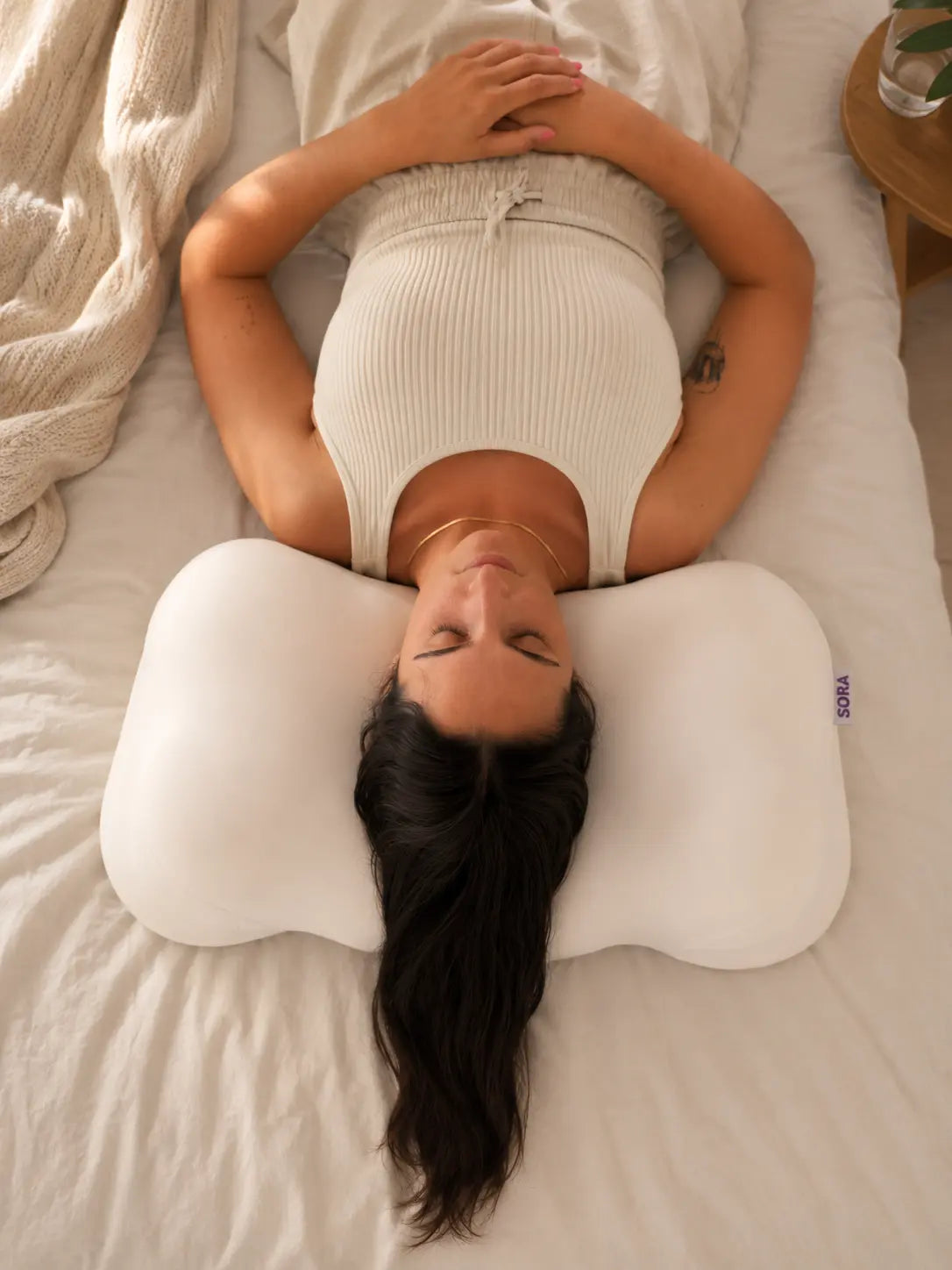 Woman sleeping on her back on SORA Cloud ergonomic pillow — top view showing contoured shape cradling head and neck for back sleeper support