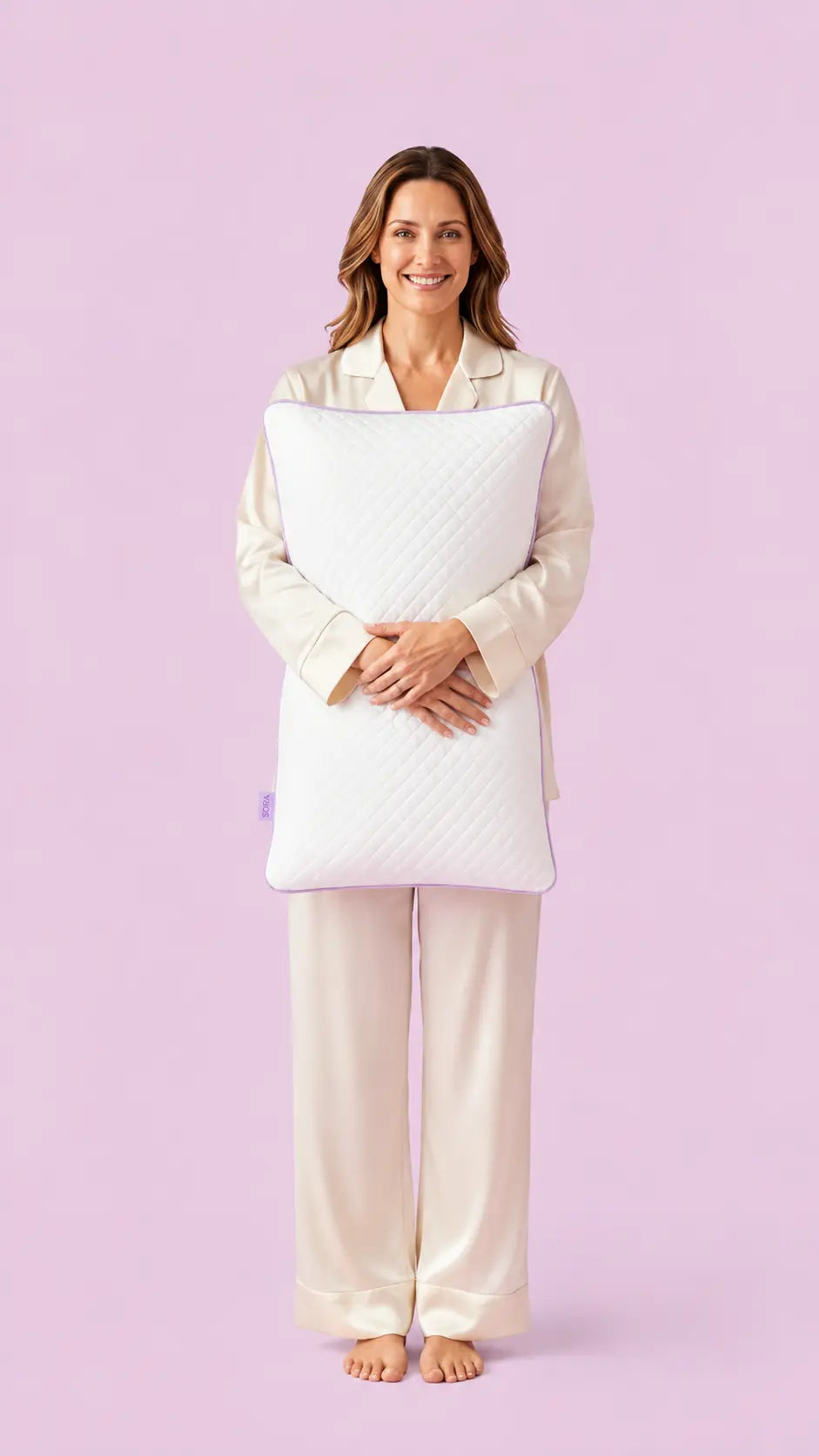Woman in pyjamas holding the SORA Adjust ergonomic pillow — lifestyle image on lavender background