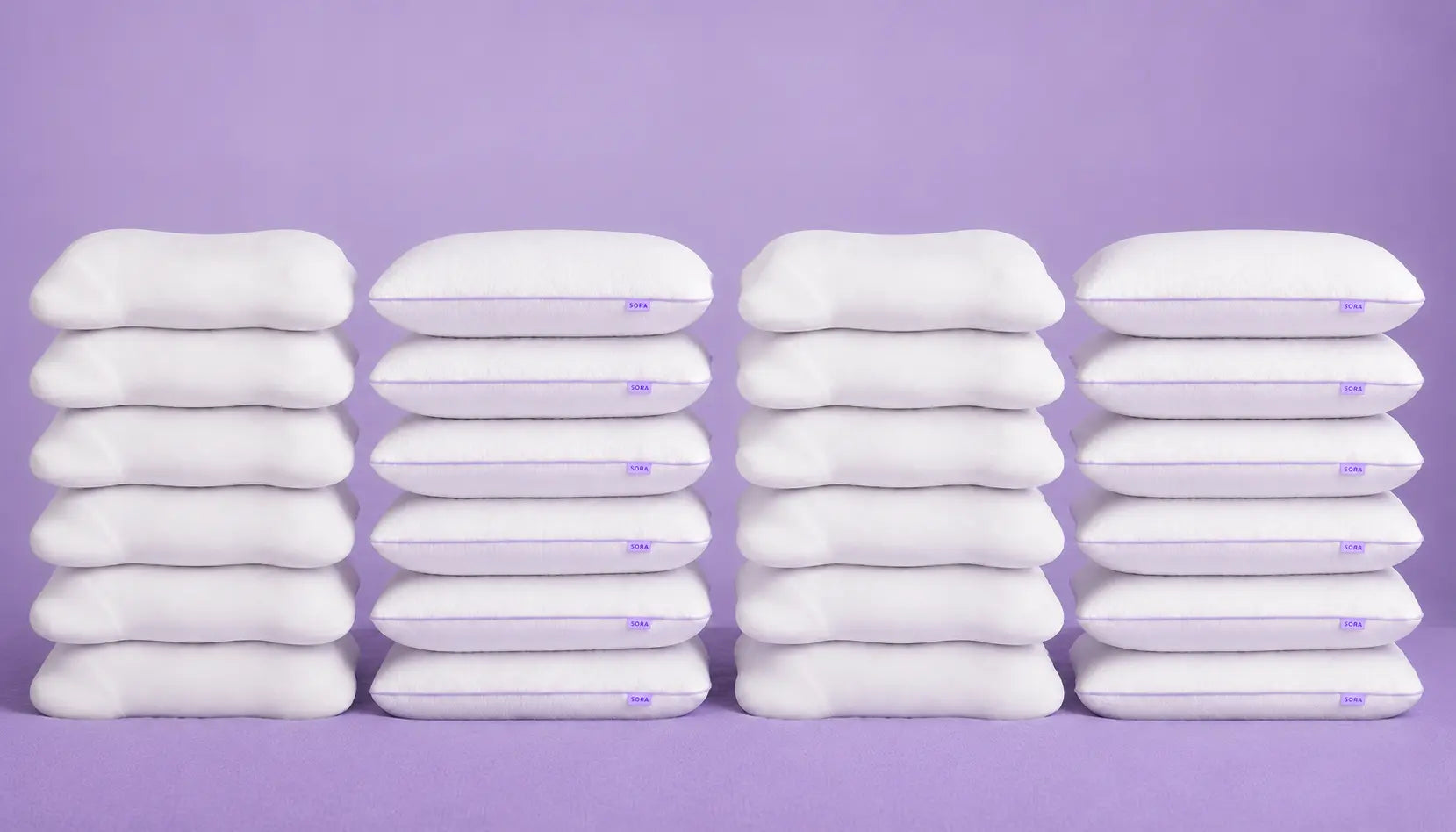 Multiple stacks of SORA Cloud ergonomic pillows on purple background — banner image showing scale of SORA sleep products