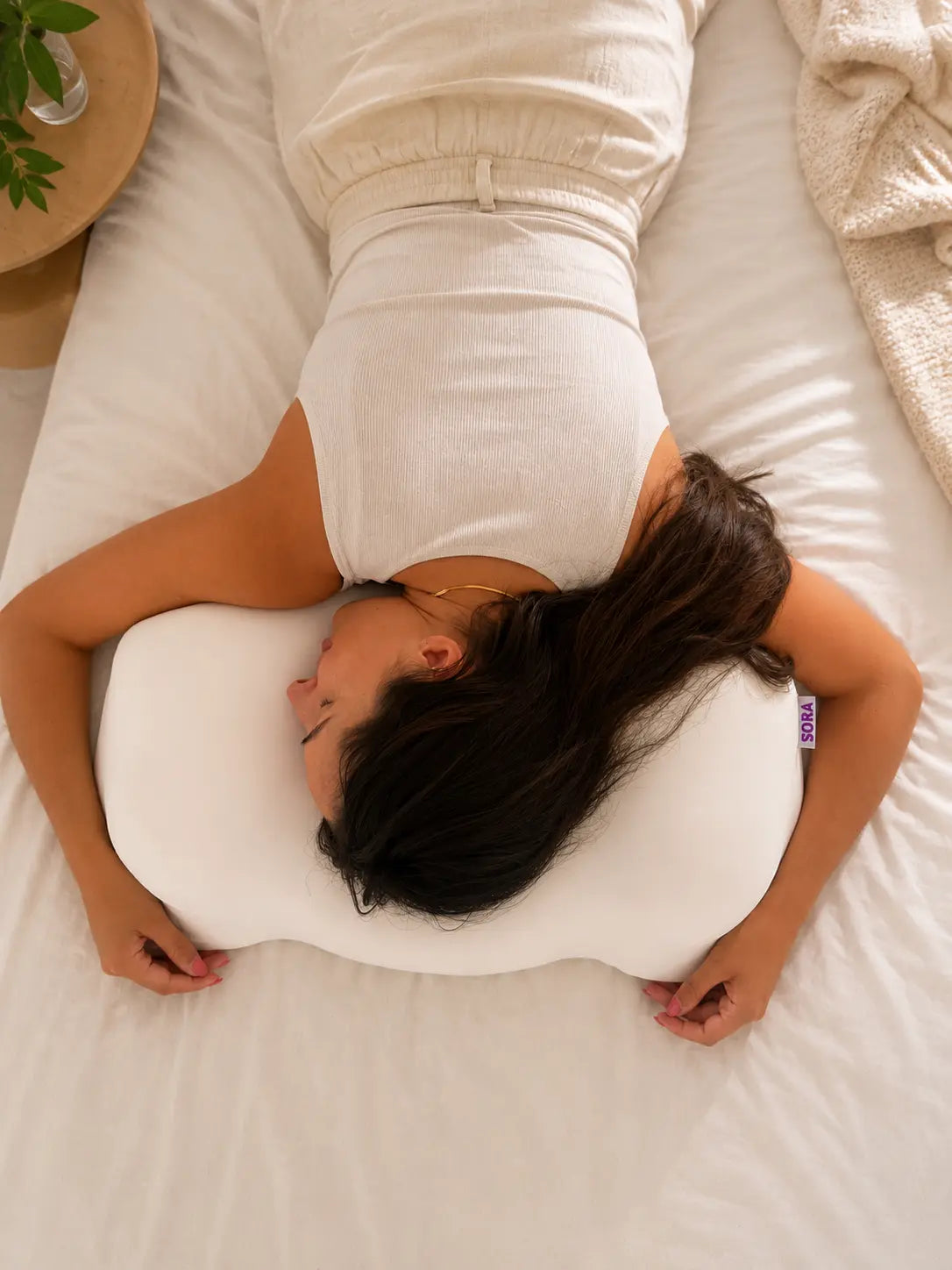 Woman sleeping on her side on SORA Cloud ergonomic pillow — top view showing contoured bone shape supporting neck and head alignment