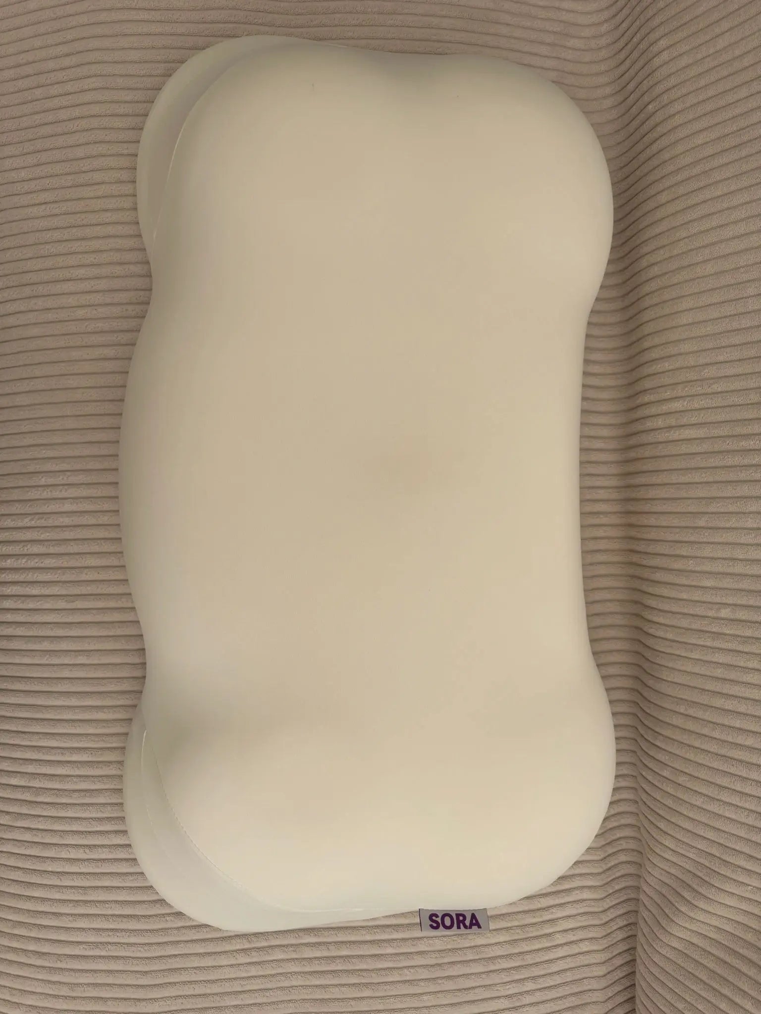 Real customer photo of the SORA Cloud ergonomic pillow on a ribbed textile surface — user-generated content showing bone-shaped memory foam pillow with SORA label