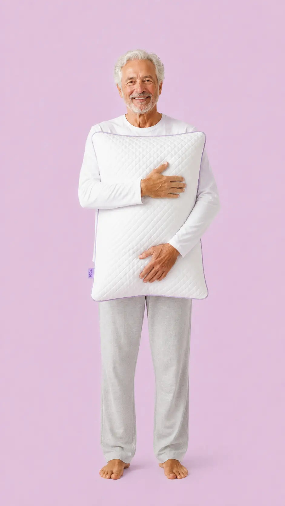 Older man in pyjamas holding the SORA Adjust ergonomic pillow — lifestyle image on lavender background