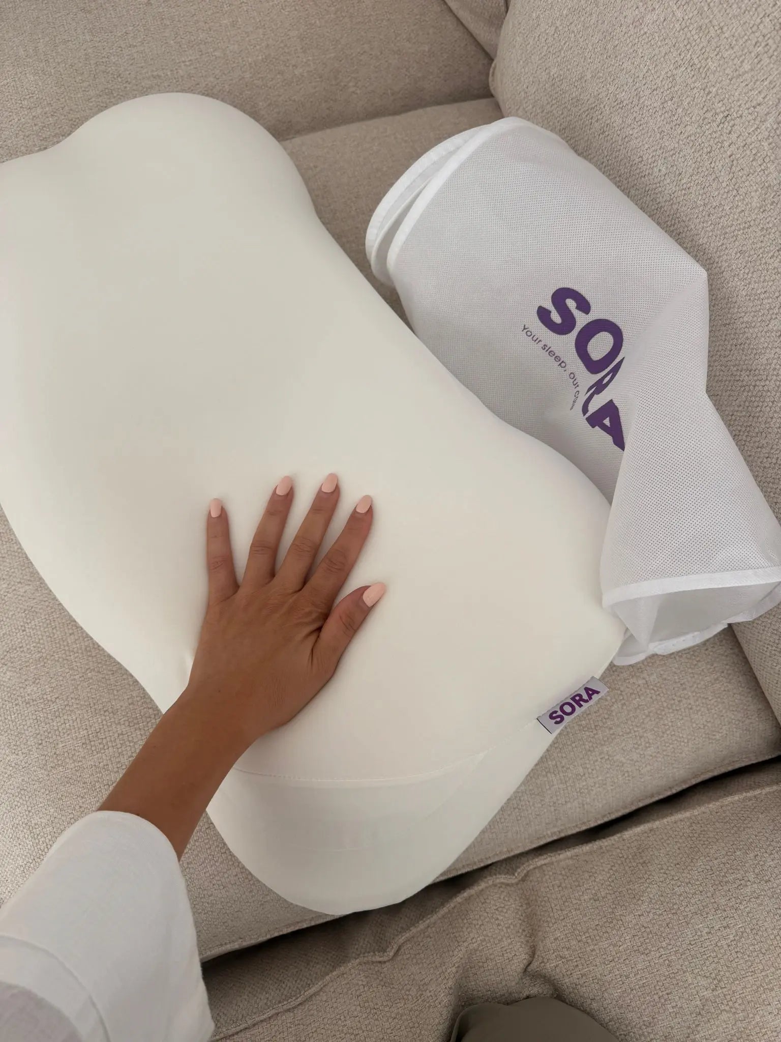 Real customer photo of SORA Cloud ergonomic pillow unboxing — hand touching bone-shaped memory foam pillow next to SORA branded packaging