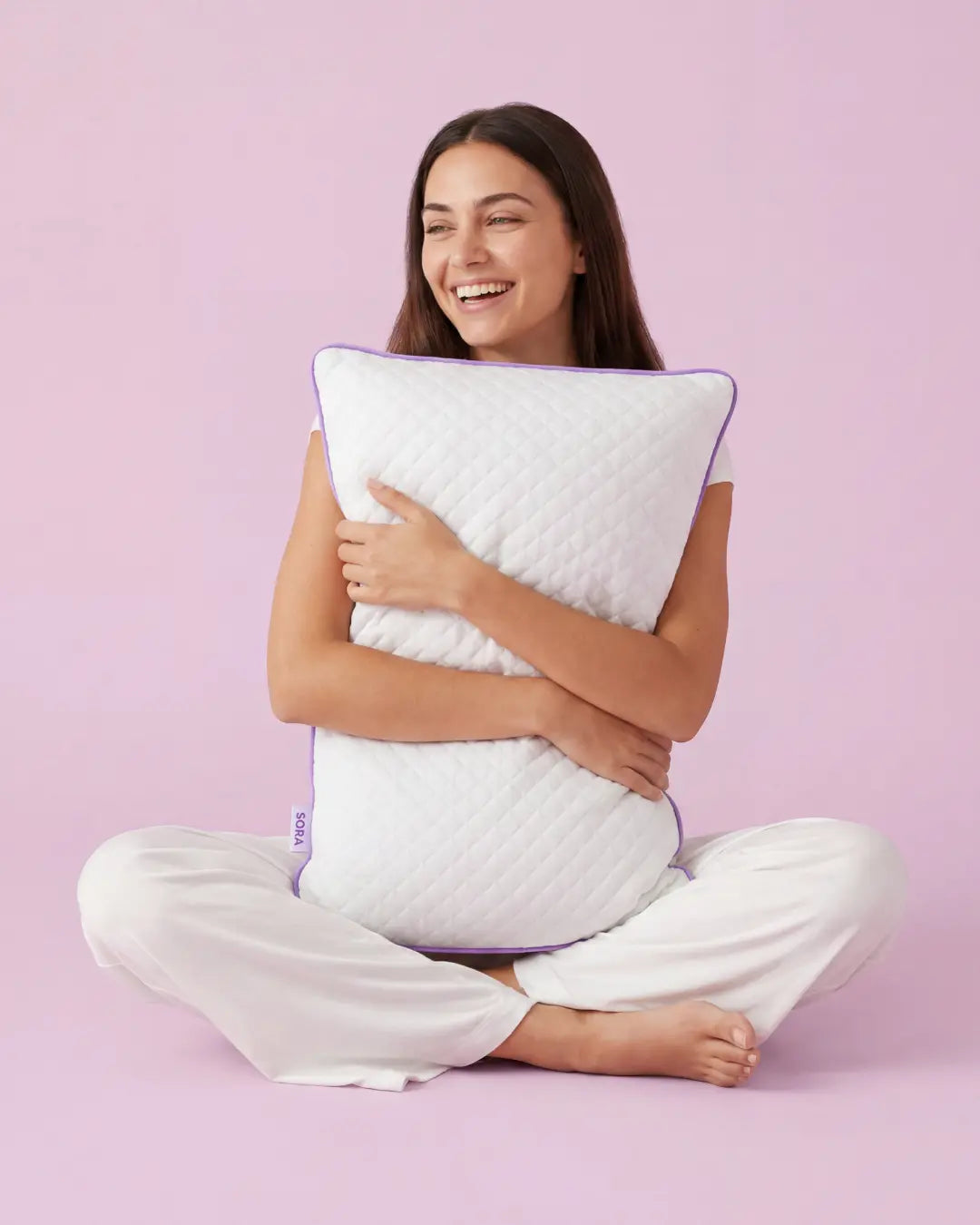 Woman hugging SORA Adjust ergonomic pillow on lavender background — lifestyle image for social media